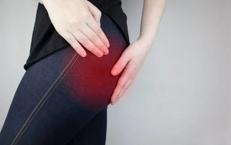 Person wearing dark jeans holding upper thigh with red area indicating piriformis syndrome hip pain