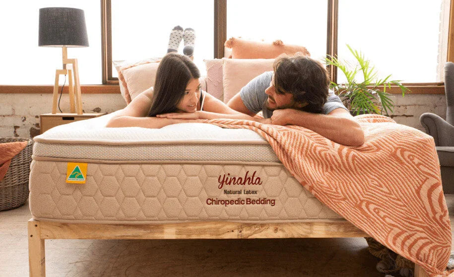 Couple lying on a yinahla natural latex chiropractic bedding mattress with orange patterned blanket in a bright bedroom