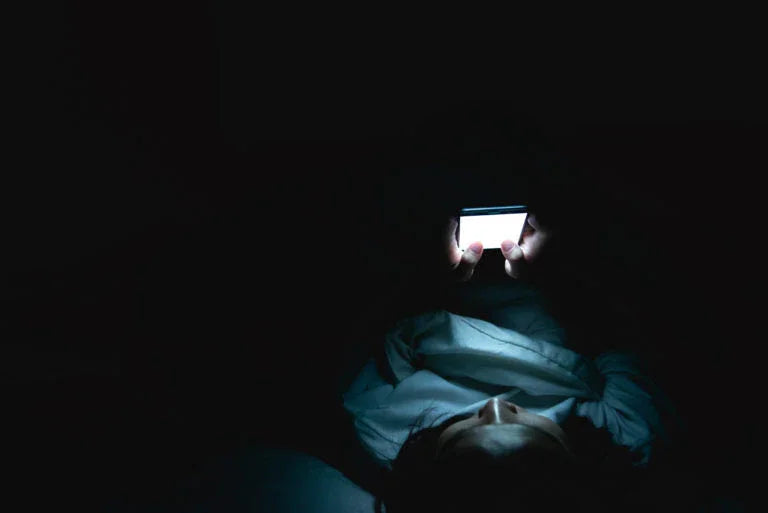 Person lying in bed in darkness illuminated by a glowing smartphone screen