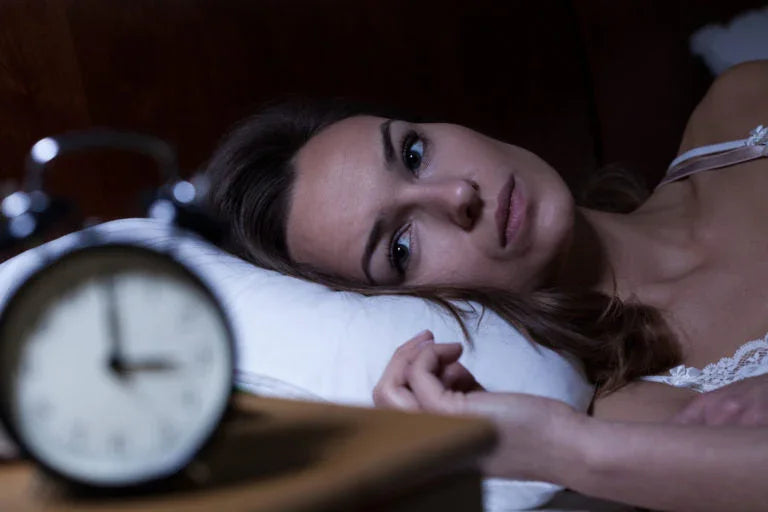 Woman lying awake in bed at night with a blurred alarm clock in the foreground